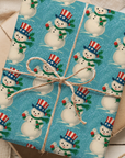 Gift wrapped in blue paper with snowman pattern, tied with brown string on a wooden surface.
