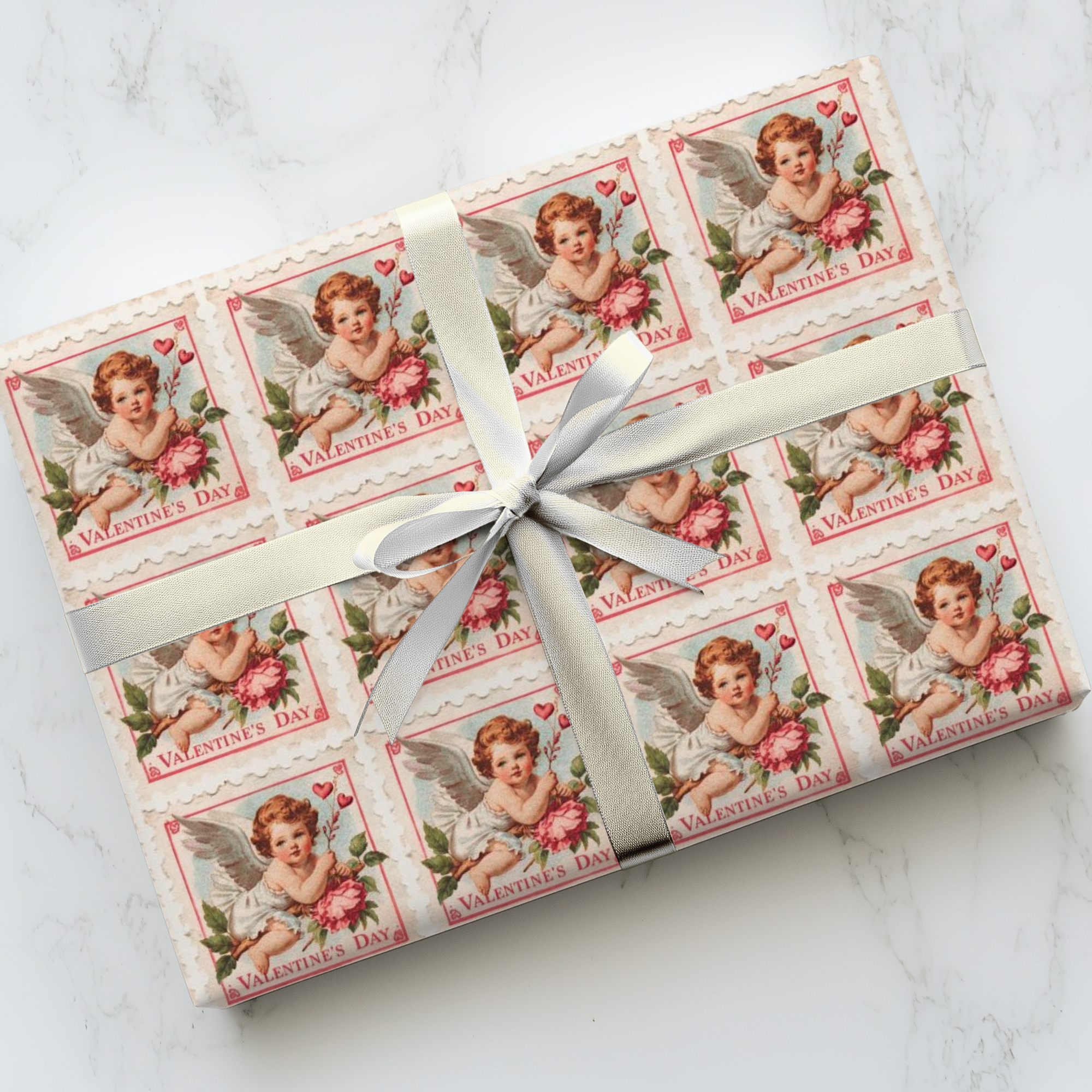 Gift wrapped in Valentine's Day-themed paper with cherub stamp illustrations on a white marble surface.