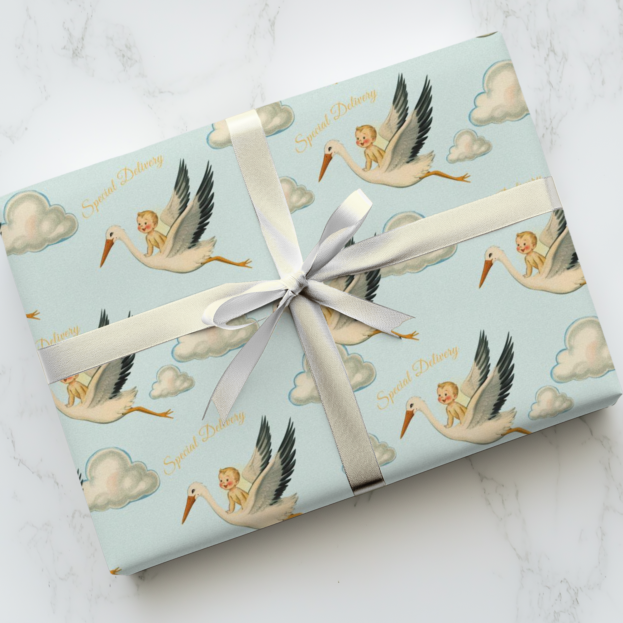 Gift wrapped in blue paper with baby and stork design on a white marble surface