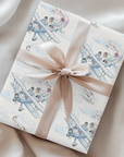 Watercolor wedding wrapping paper with a just married vintage biplane design, tied with a champagne satin ribbon on a neutral draped background.