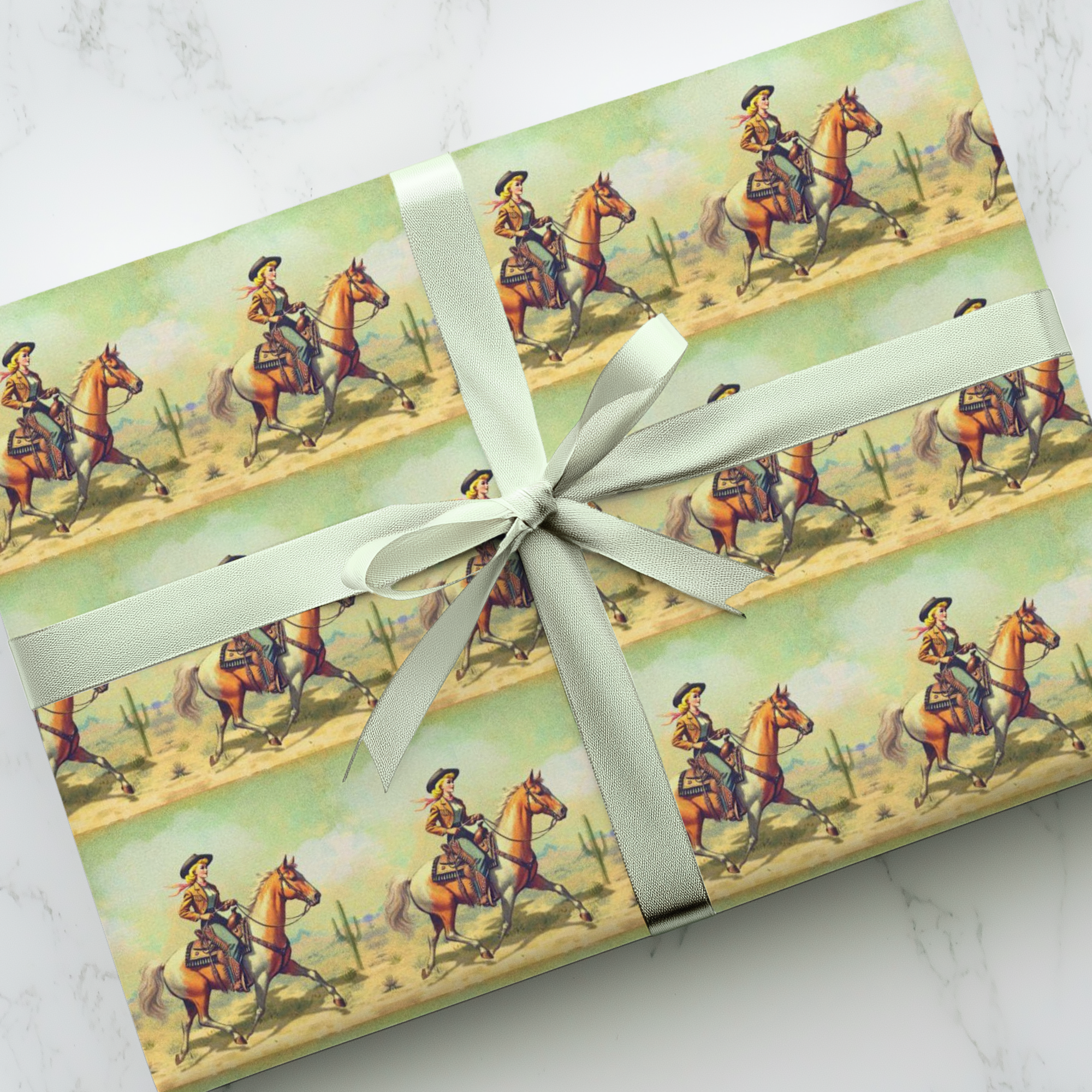 Gift wrapped in cowgirl-themed paper with a white ribbon on a marble surface